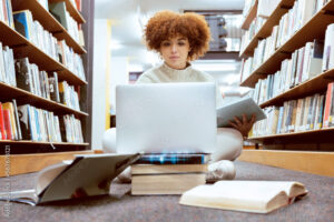 estudiante con libros y computadora en biblioteca
